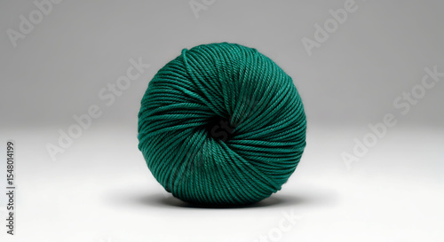 A neatly rolled ball of dark green yarn sits on a glossy white surface with soft lighting, showcasing its smooth texture and tightly wound fibers. The focus highlights its symmetrical shape