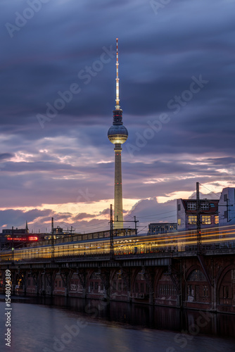The famous Television Tower and the river Spree with a motion blurred commuter train in Berlin at twilight