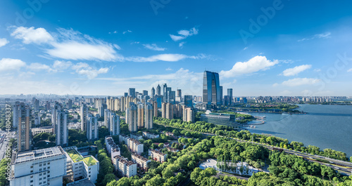 Fototapeta Naklejka Na Ścianę i Meble -  Modern city commercial buildings with green park and a large lake under a bright blue sky in Suzhou, China.