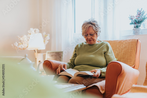 Schilderij op canvas A mature woman enjoying a book in a comfortable armchair, surrounded by a warm and inviting atmosphere with soft lighting and homely decor