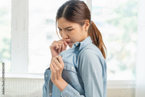 Smelly clothes laundry, housewife woman having bad smelling clothes on the hand holding breath nose with finger, sniff smelly dirty stinky musty and look disgusting.