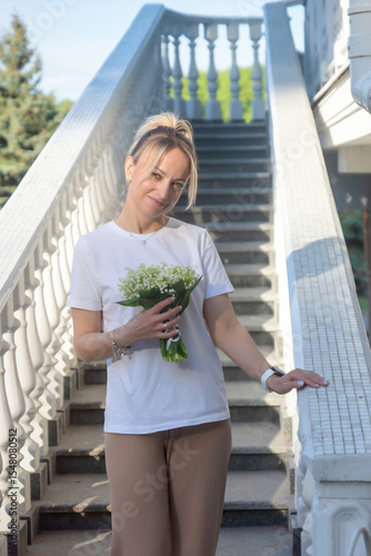 A young, beautiful girl with a bouquet of lilies of the valley on a walk.