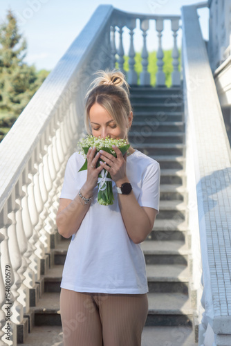 A young, beautiful girl with a bouquet of lilies of the valley on a walk.