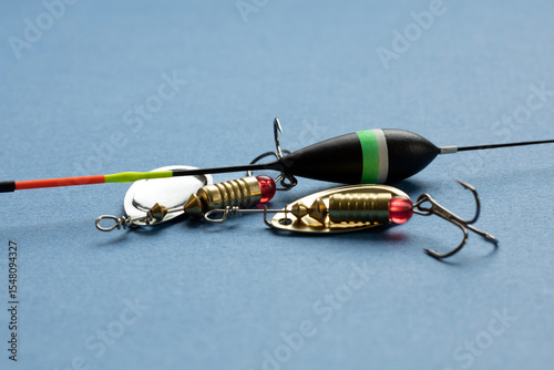 Fishing tackle including a float and lures on a blue background. The float is black with green and red accents. Lures are shiny with hooks.