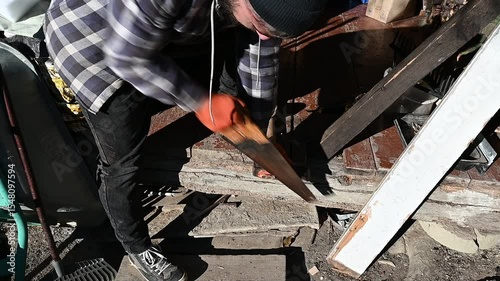 Focused on his craft, a skilled carpenter works diligently in an outdoor workshop, using a hand saw to shape wooden materials in the warm afternoon sun, makes an axe handle.