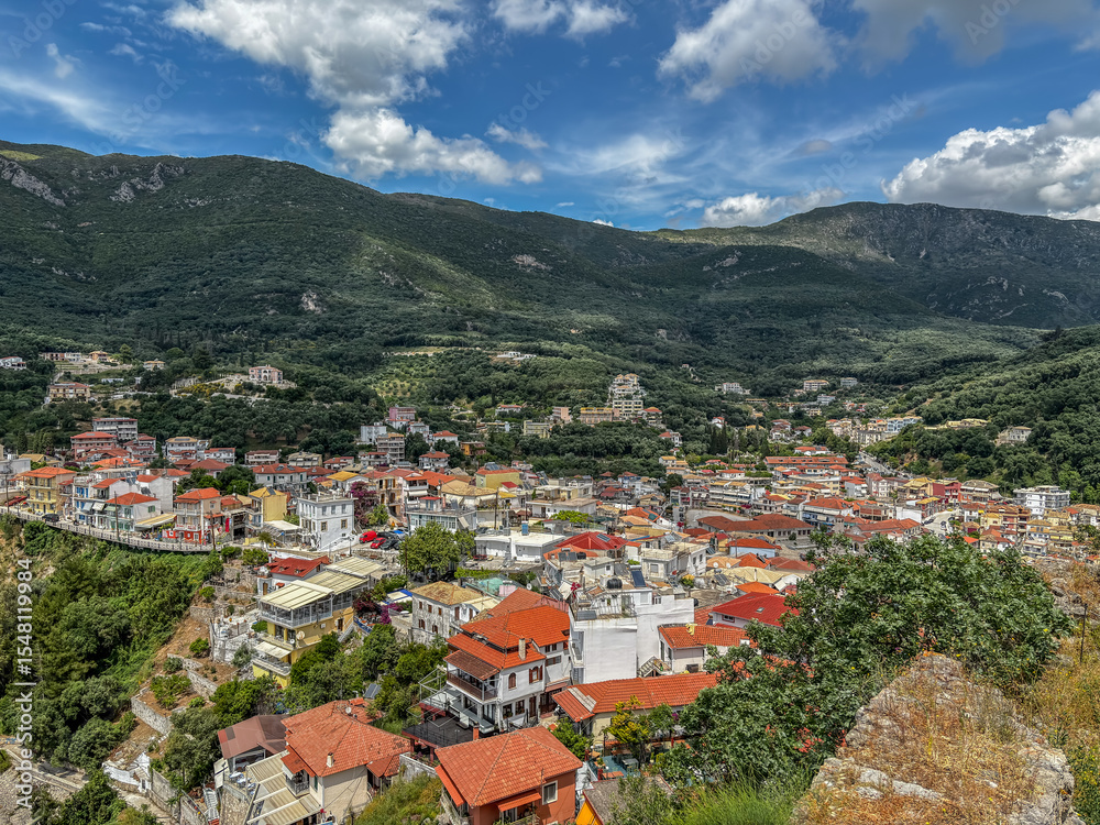 Obraz premium Panoramic view of Parga, a picturesque coastal town in Greece, famous for its colorful houses with red-tiled roofs nestled in a lush green mountain valley.