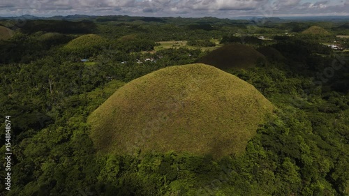 A lone majestic Chocolate Hill emerges from a thick green forest Among Dense Jungle in sunny cloudy day, Bohol, Philippines