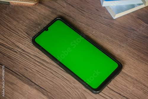 Green screen smartphone on wooden table with books & notebooks. Ideal for mockups & tech concepts.
