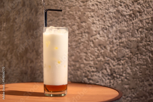 A glass of white milk and a black straw are on the round wooden table.
