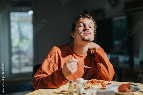 Obraz na plátně A young man wearing an orange sweater delighting in a meal served on a checkered table