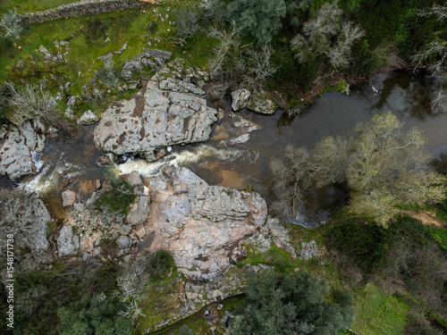 A small stream flows between rugged rocks in a natural landscape, capturing the peaceful movement of water in a wild, untouched environment.