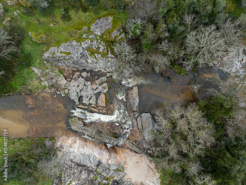 A small stream flows between rugged rocks in a natural landscape, capturing the peaceful movement of water in a wild, untouched environment.