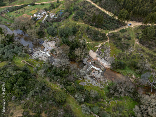 A small stream flows between rugged rocks in a natural landscape, capturing the peaceful movement of water in a wild, untouched environment.