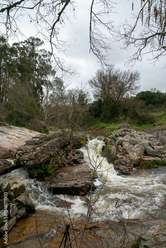 A small stream flows between rugged rocks in a natural landscape, capturing the peaceful movement of water in a wild, untouched environment.