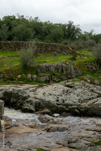 A small stream flows between rugged rocks in a natural landscape, capturing the peaceful movement of water in a wild, untouched environment.