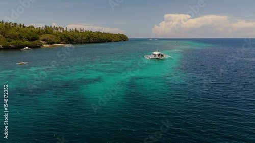 Traditional Bangka Boats and kayaks Near Coral turquoise Waters and tropical palm tree island in Pamilacan Island, Panglao, Bohol, Philippines