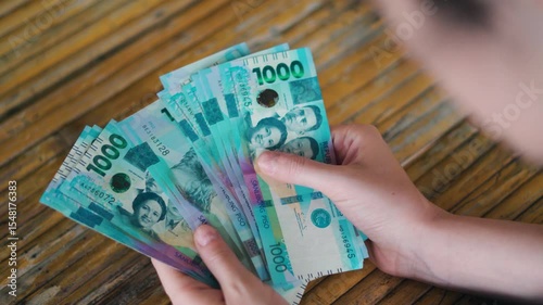 Overhead Shot of a Person Counting and Organizing Stacks of New Philippine 1000 Peso Polymer Banknotes on a Weathered Yellow Wooden Surface – Focus on Hands and Financial Transaction