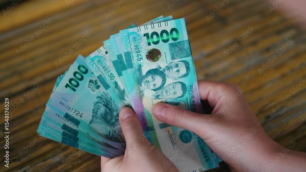 Close-up of a Person Holding and Counting New Philippine 1000 Peso Polymer Banknotes Over a Rustic Wooden Table Surface – Featuring Hands, Currency Security Details, and Filipino Historical Figures