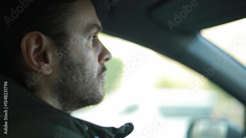 Close-up of a focused man driving a car, looking straight ahead with concentration. Daylight streams through the window, creating a calm, natural atmosphere of commuting or travel.
