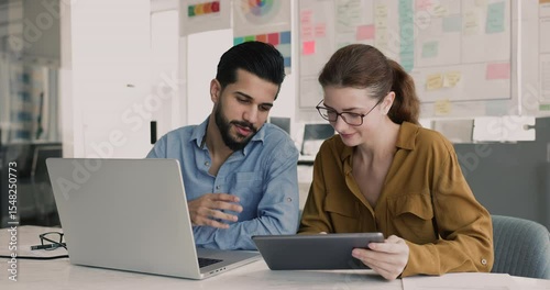 Diverse couple of company colleagues using laptop and tablet together. Friendly advisor, mentor showing work application, software on digital gadget to new employee, giving help to coworker