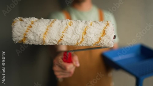 Professional painter holding new paint roller near paint tray, demonstrating painting equipment with construction worker blurred in background during home renovation project