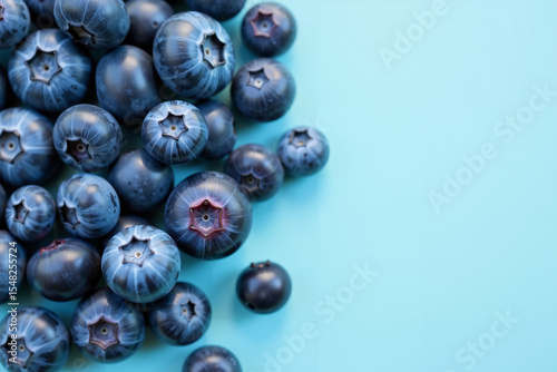 Close-up of fresh blueberries in rich shades of blue and purple scattered on a pastel blue background. Space for text.