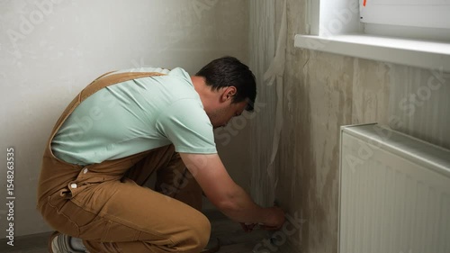 Professional handyman carefully scraping old wallpaper from wall surfaces, using specialized spatula for thorough surface preparation during apartment renovation process