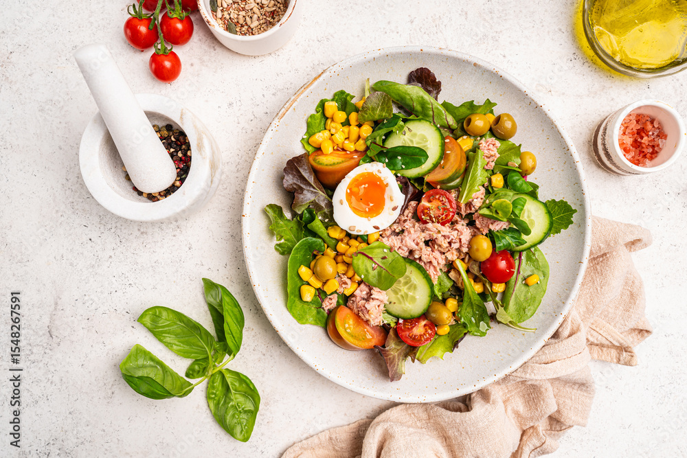 Fototapeta premium Tuna salad with tomatoes, cucumber, corn, olives , eggs and onion on white stone background, top view. High quality photo