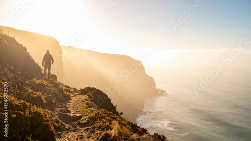 A lone figure stands silhouetted against a golden sunrise Rugged cliffs meet the vast ocean under a radiant sky Adventure awaits on this breathtaking coast