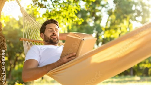 A bearded man relaxes outdoors in a hammock reading a book Sunlight filters through trees He appears peaceful enjoying a leisurely afternoon Golden light surrounds him