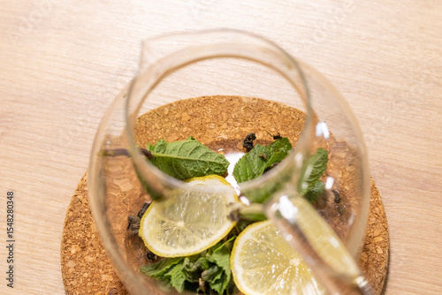 Stylish transparent tea pot with dried tea leaves, mint leaves and lemon slices in it. Beverage