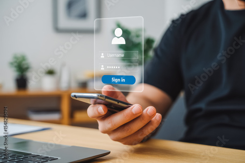 A person uses a smartphone to access a login interface, featuring username and password fields. A laptop and blurred plant in the background suggest a modern workspace environment.