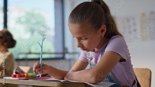 Preteen schoolgirl writing lesson in copybook sitting class desk closeup. 