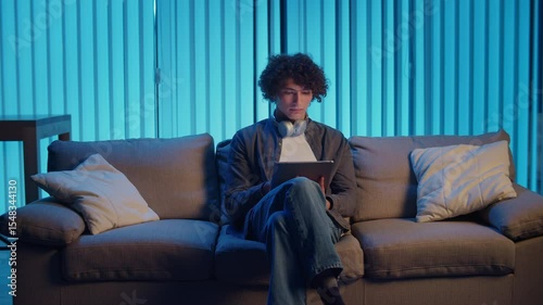 Man Relaxes on Sofa Using Tablet, Possibly Watching Streaming Content or Reading. Everyday Self-Care and Slow Living in the Digital Age. Digital Detox, Mental Health, Focus Mode.
