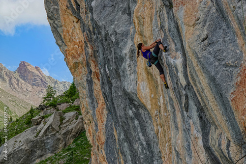 LOW ANGLE VIEW: Climber on a difficult section of a streaked, layered rock face. Stunning alpine mountain backdrop provides a magnificent setting for this demanding yet rewarding athletic endeavour.