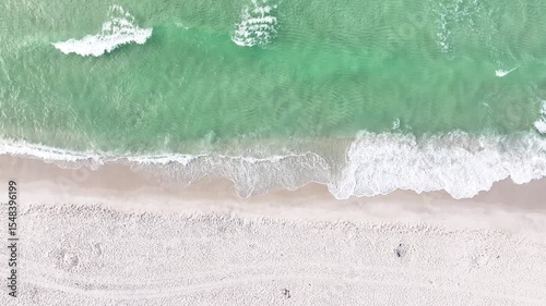 Slow-motion video of a birds-eye-view of ocean waves crashing onto a sandy beach in Pensacola, Florida, on a beautiful sunny summer day