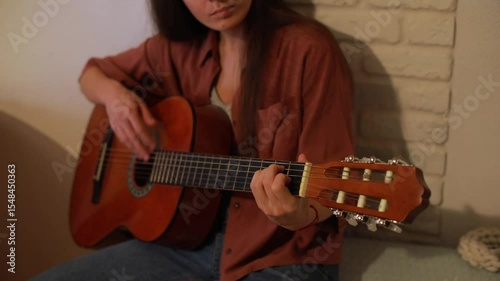 Close-up of a young woman playing acoustic guitar at home. Focus on hands and strings, showing practice, concentration, and the intimate process of learning or composing music.

