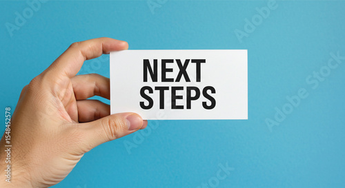 Next Steps: A Hand Holds Up a Sign with "Next Steps" Text Displayed Against Blue Backdrop, Emphasizing Progress