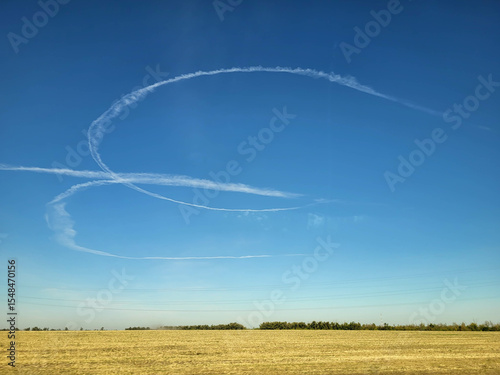 White traces of an airplane in the blue sky above the field