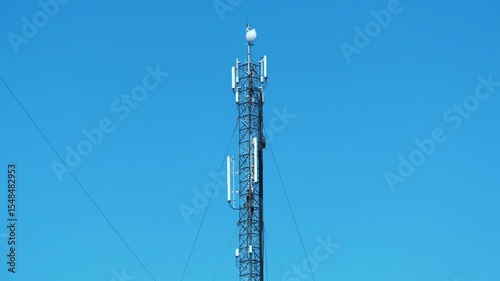 Worker climbs up a mobile phone tower. Two workmen on cell tower. High-altitude work. Cell tower on blue background. Maintenance staff at work. Repairmen service a cell tower, install new equipment