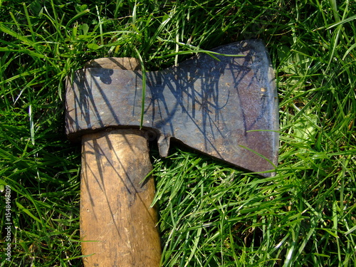 Rustic axe resting on lush green grass, showcasing its weathered blade and wooden handle, highlighting craftsmanship and outdoor tools in a natural setting