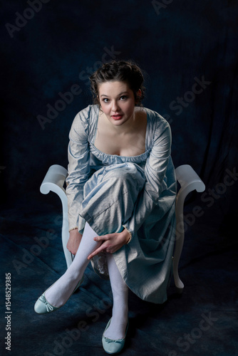 A Regency woman wearing a blue cotton dress and sitting on a wooden seat
