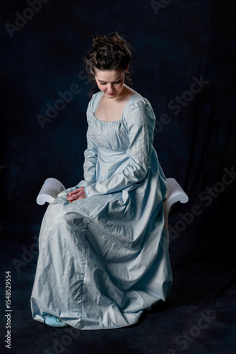 A Regency woman wearing a blue cotton dress and sitting on a wooden seat