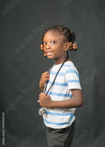 Adorable Nigerian girl in casual wear with a stethoscope around her neck, playfully portraying future medical ambition and childhood imagination.