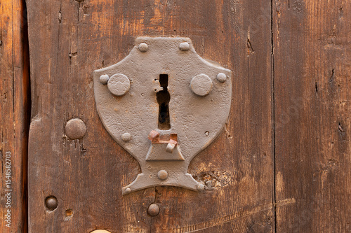 Old metal keyhole surround embedded into a weathered wooden door