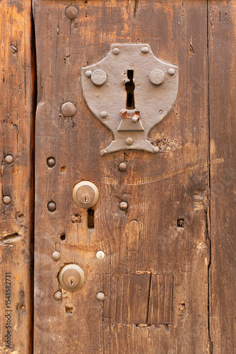 Old metal keyhole surround embedded into a weathered wooden door
