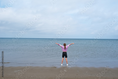 A girl doing yoga, standing on the beach, spreading her arms wide. The scene captured a moment of freedom and openness with the sea,