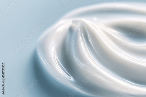 Close-up of smooth glossy white cream or gel with rich texture and shiny reflective surface arranged in elegant swirls on light blue background
