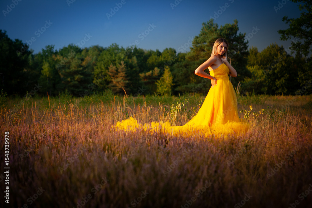 Obraz premium A stunning and graceful model dressed in a flowing yellow gown stands proudly amidst a tranquil wildflower field