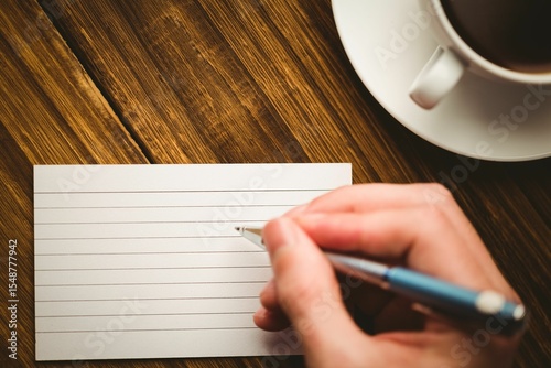 Human hand writing on paper at desk with coffee cup